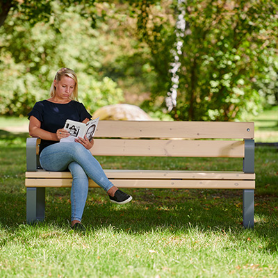 Eine Frau entspannt sich in einem Park auf einer Holzbank und liest ein Buch.